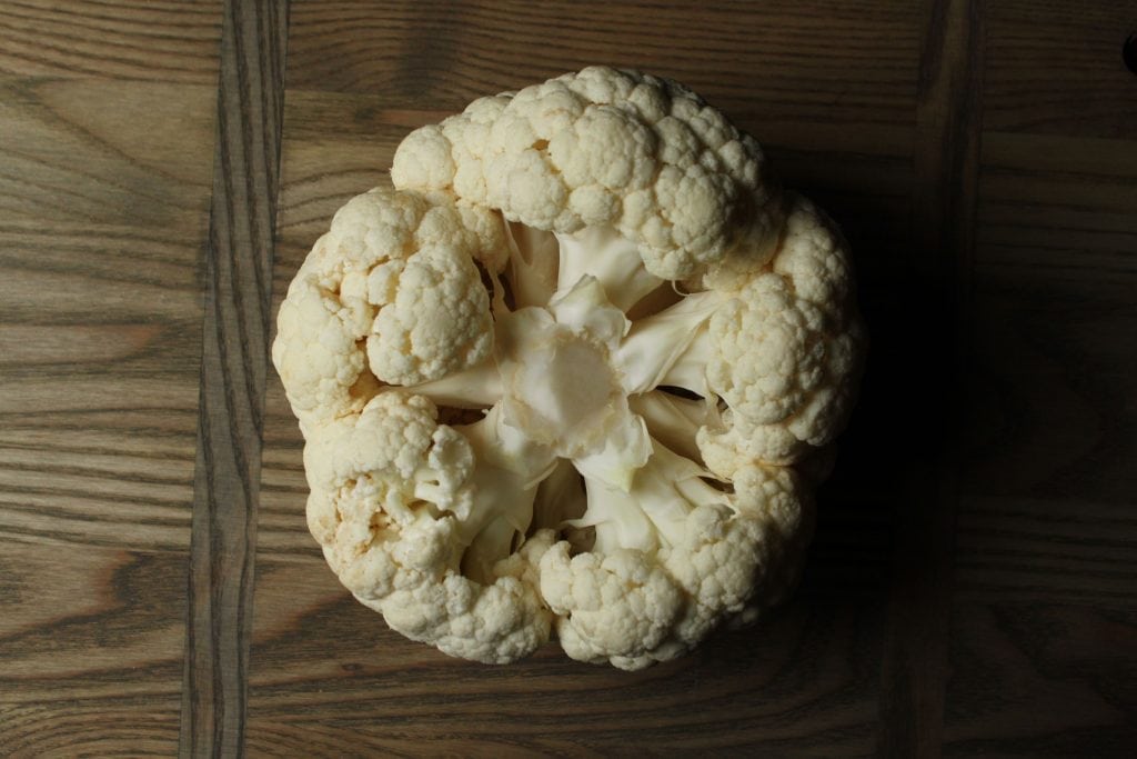 Whole Roasted Cauliflower - A raw cauliflower on a wooden board.