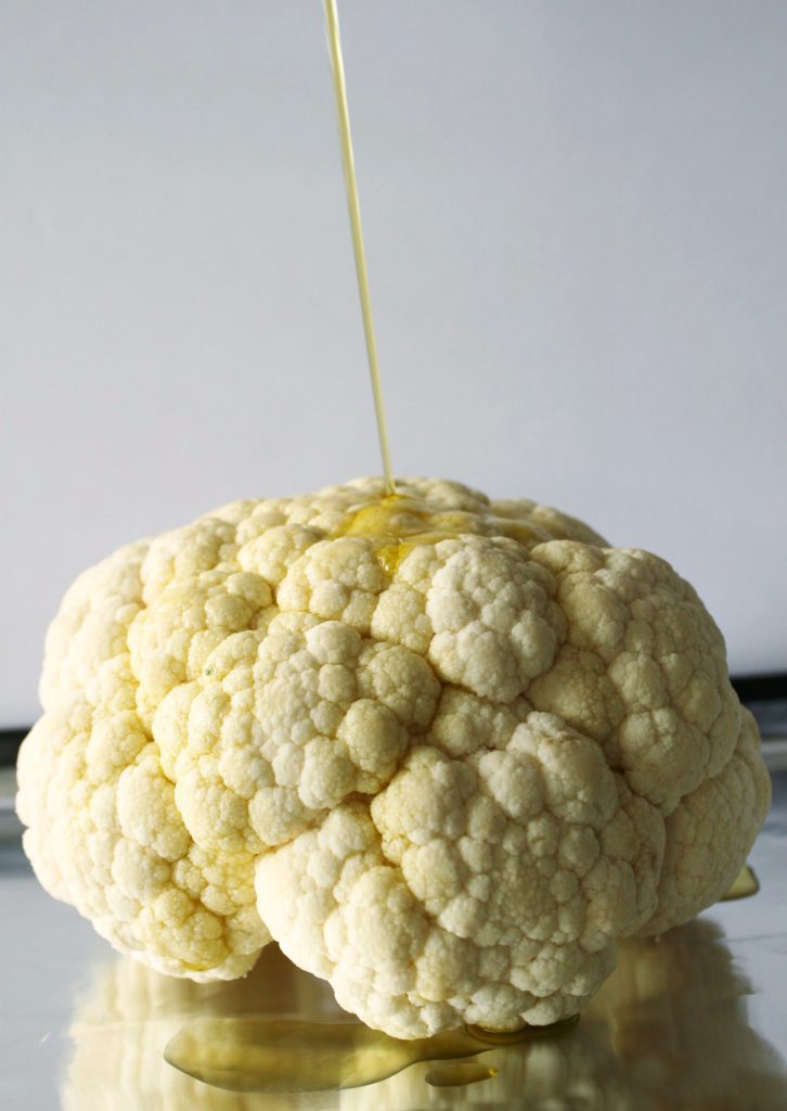 Whole Roasted Cauliflower - a raw whole cauliflower being drizzle in olive oil. 