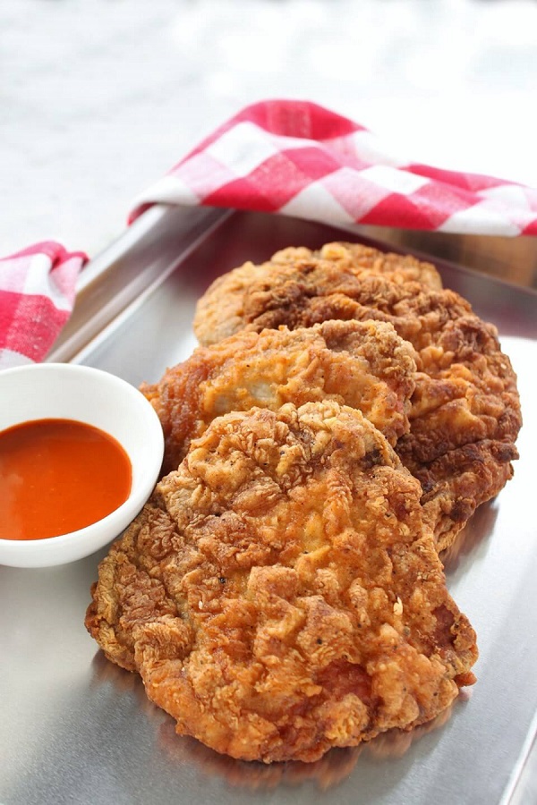 Country Fried Pork Chops - Dish 'n' the Kitchen Three golden fried pork chops on a platter with a side of orange hot sauce.