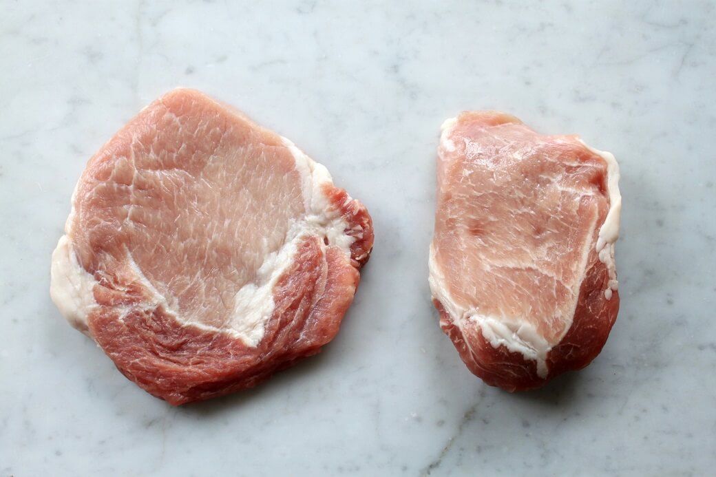 Country Fried Pork Chops - Dish 'n' the Kitchen Three raw pork chops on a white backdrop.