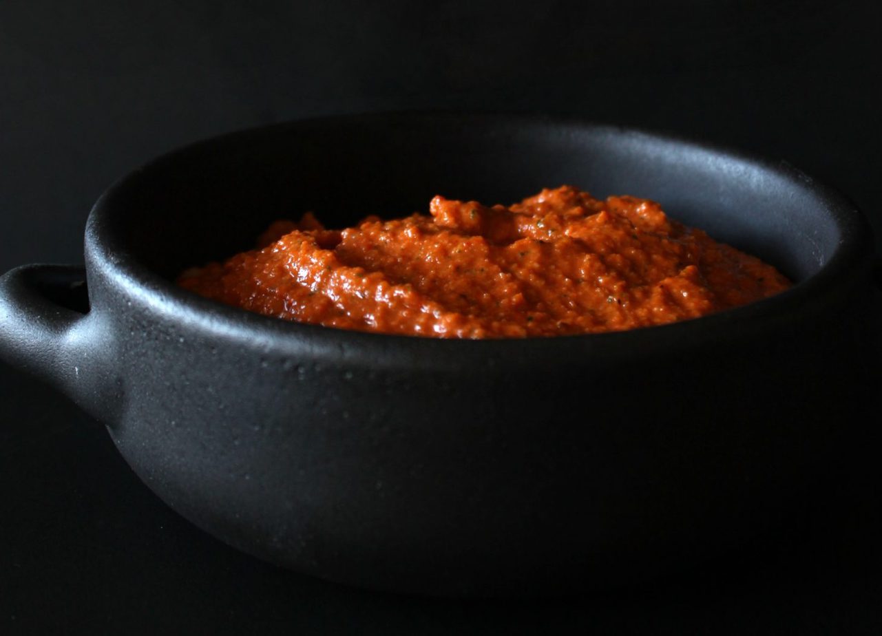 Romesco Sauce - A bright orange sauce in a black bowl against a black background.