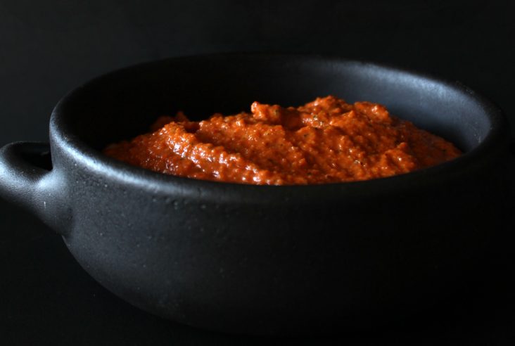 Romesco Sauce - A bright orange sauce in a black bowl against a black background.