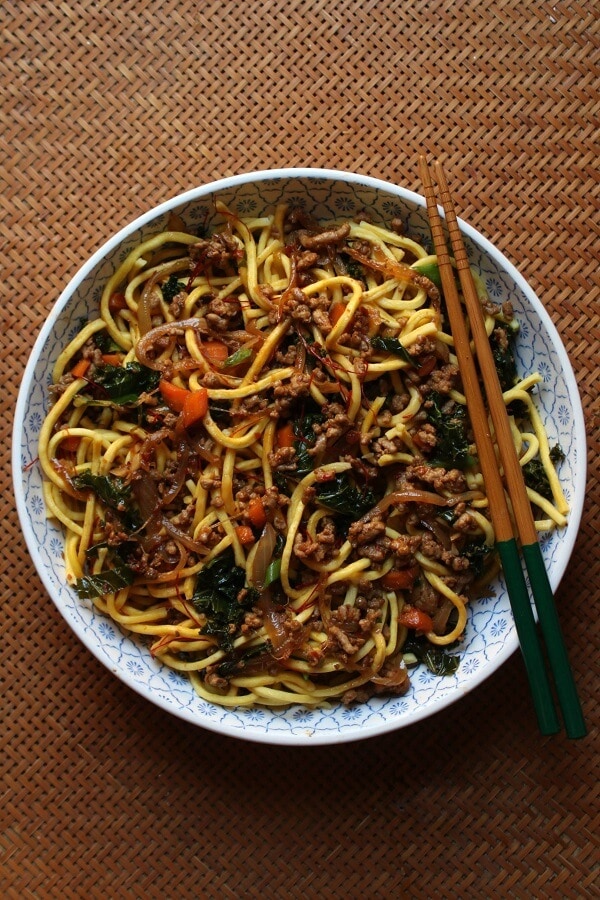 A bowl of noodles mixed with ground pork, carrots, kale, and green onions. 