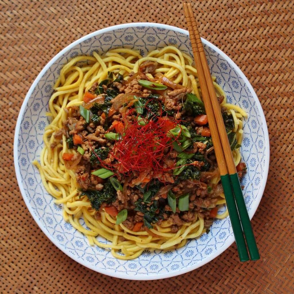 A bowl of noodles topped with ground pork, carrots, kale, and green onions. 