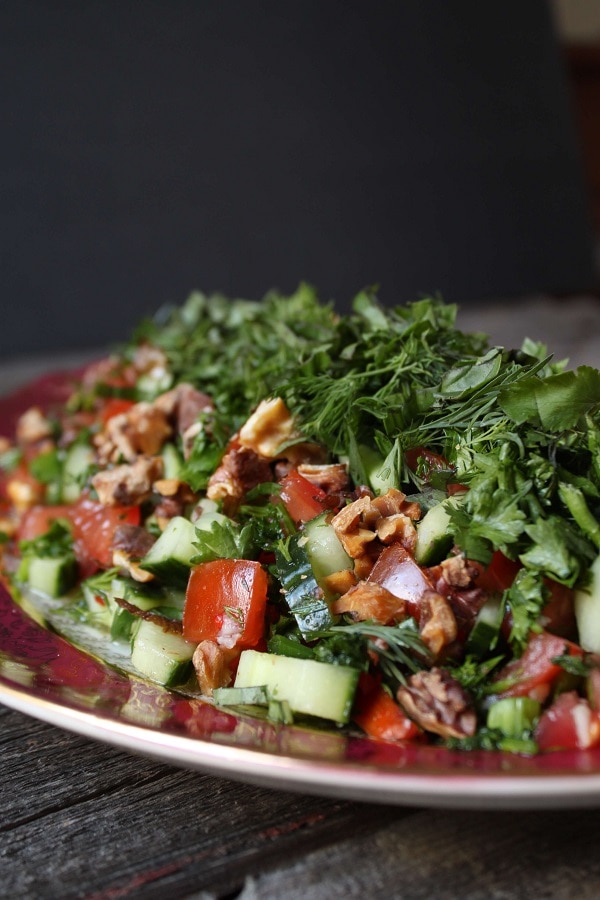 A platter containing a fresh salad of cucumbers, tomatoes, walnuts, and fresh herbs.