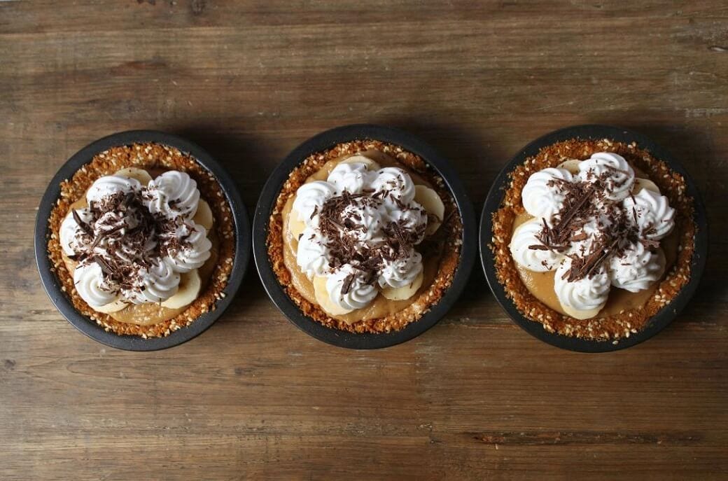 Three mini banoffee pies in a line on a wooden table