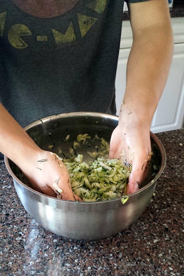 A person massaging fresh dill and cabbage together in a stainless steel bowl. 