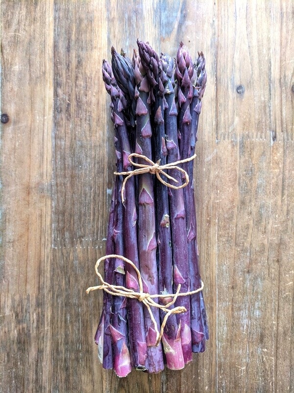 A bunch of purple asparagus tied with a string sitting on a purple background. 