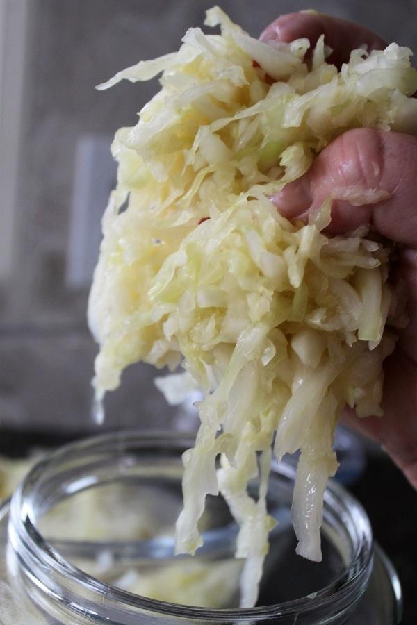 A hand lifting wet cabbage from a jar. 