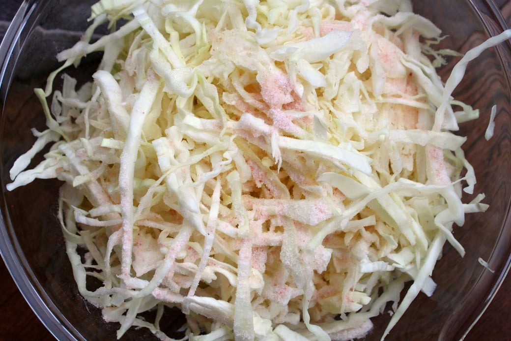 A bowl of shredded green cabbage with pink Himalayan salt sprinkled on top. 