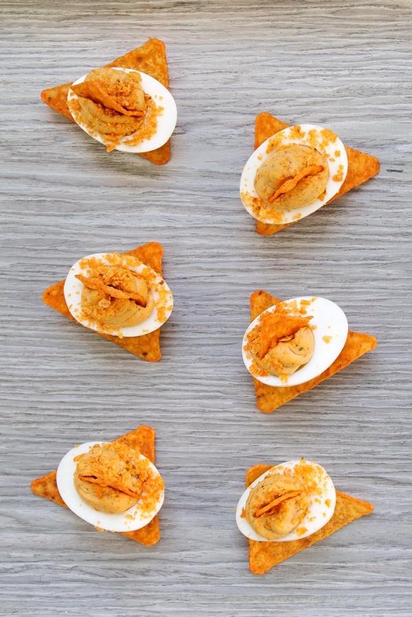 Nacho Deviled Eggs topped with Dorito crumbs on a grey wooden background. 