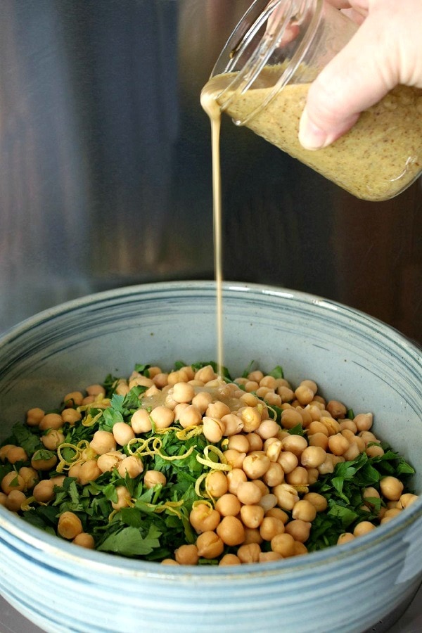 A hand drizzles tahini salad dressing onto a salad in a blue bowl. 