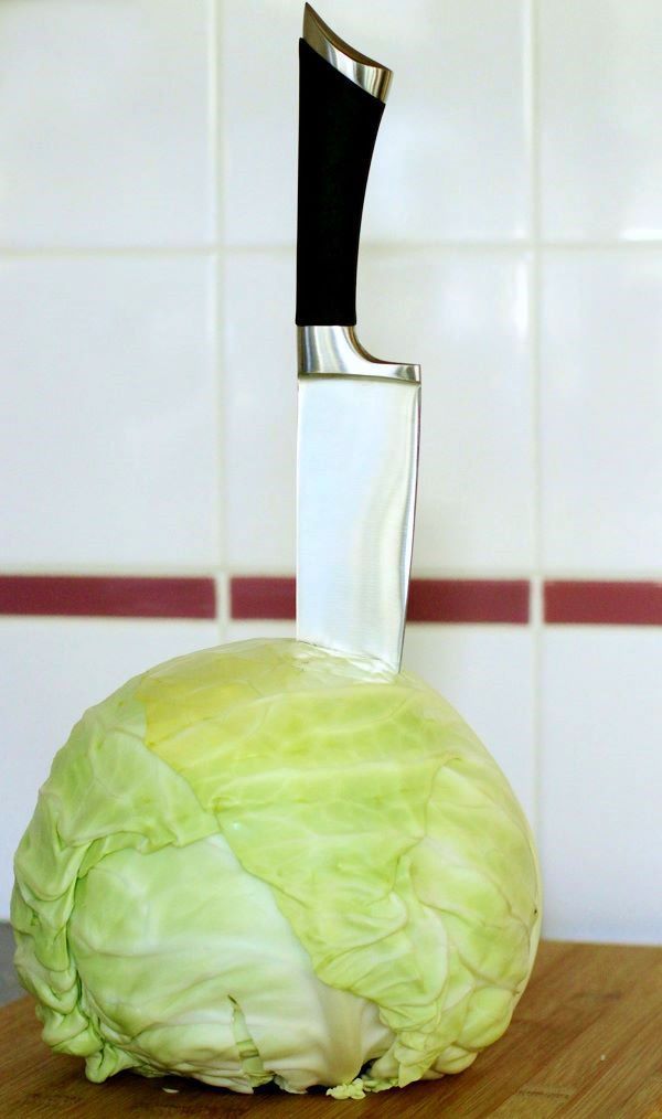 A whole green cabbage with a knife stuck in the top.