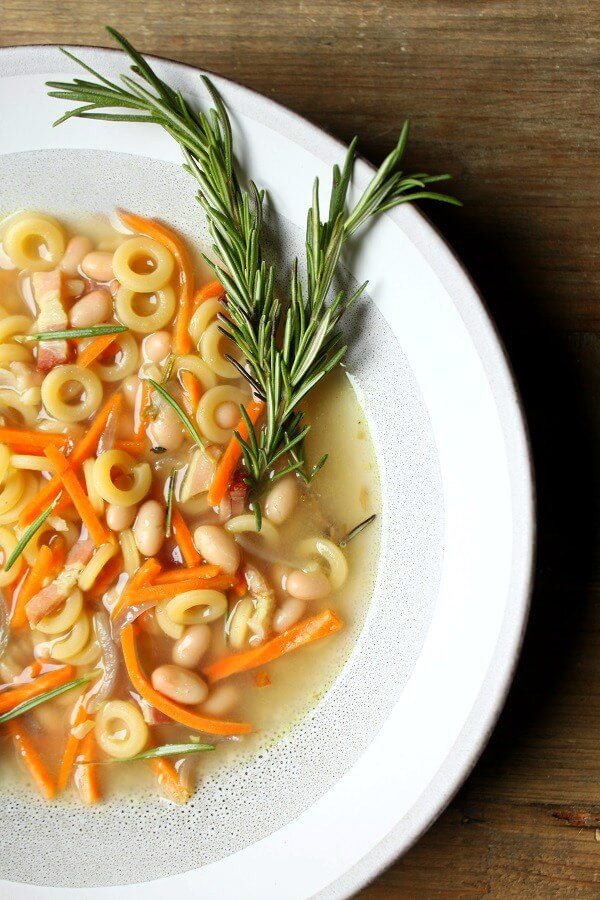 Vertical image of a bowl of Pasta e Fagioli noodle soup with bacon and carrots. 