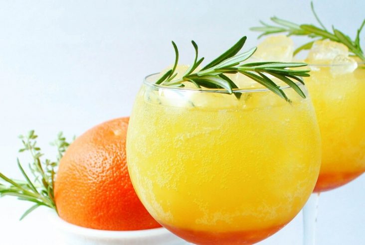 Two bright orange icy drinks garnished with fresh rosemary.