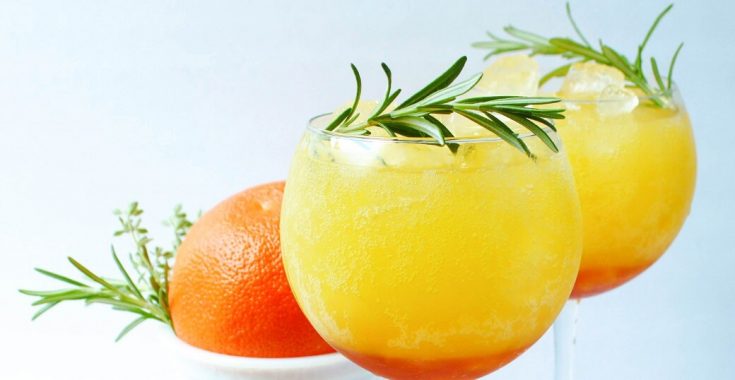 Two bright orange icy drinks garnished with fresh rosemary.