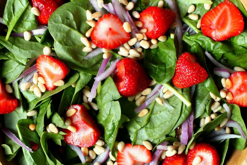 Spinach Salad with green baby spinach leaves, red strawberries, pine nuts, and red onions. 