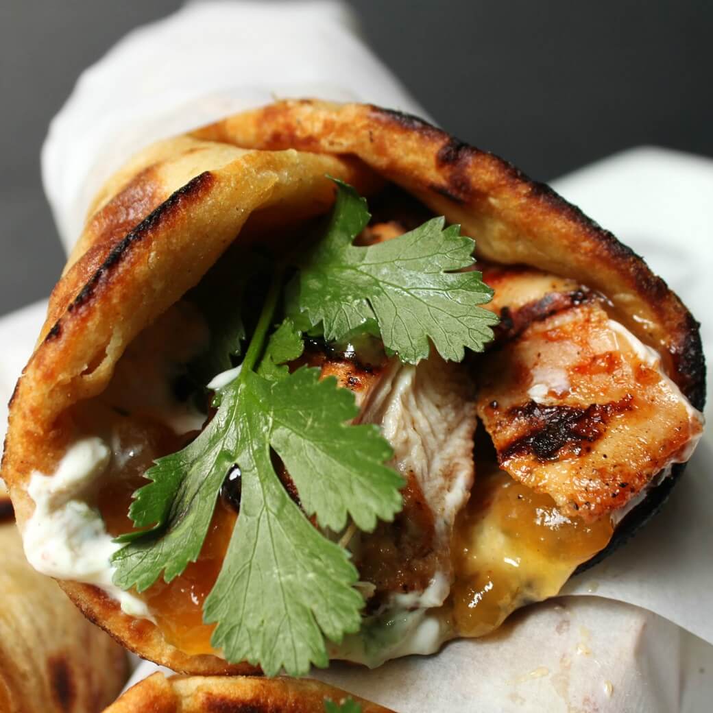 close up of grilled chicken wrapped in paratha along with cilantro, mango chutney, and raita.