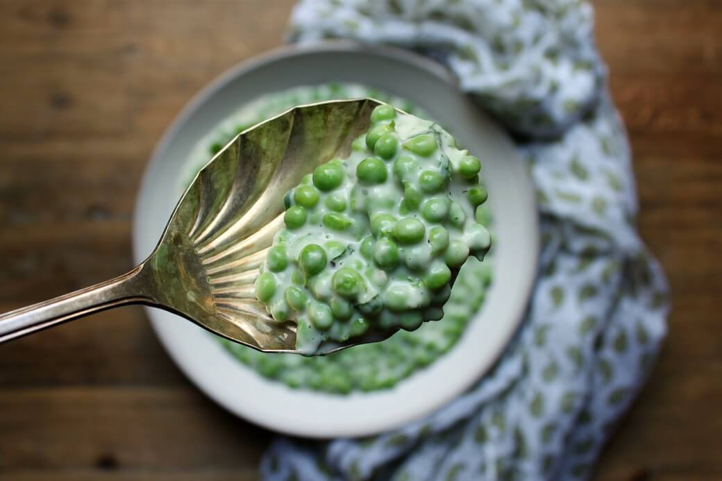 Close up of green peas in a cream sauce on an antique scalloped silver spoon.