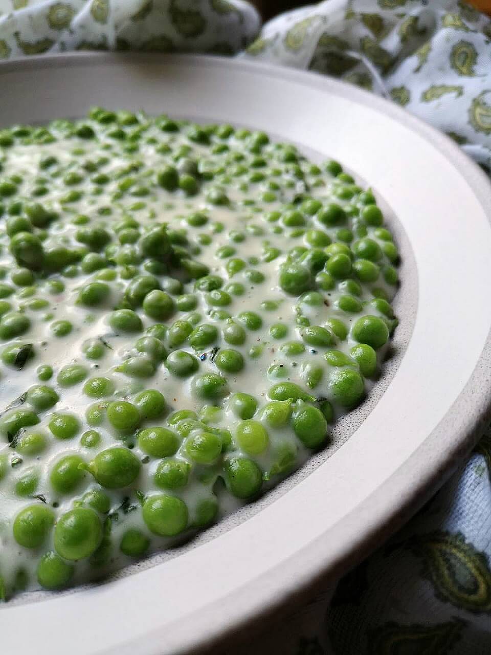 A bowl of green peas in a creamy sauce.