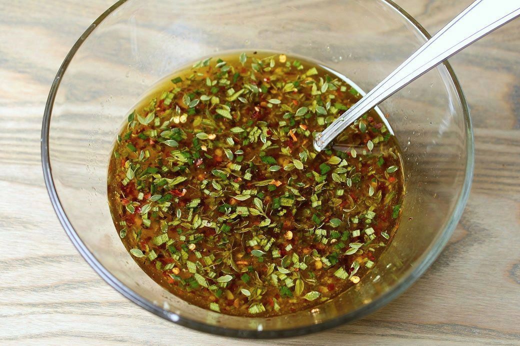 A bowl of marinade containing chili flakes, fresh green herbs, garlic, olive oil, and vinegar.