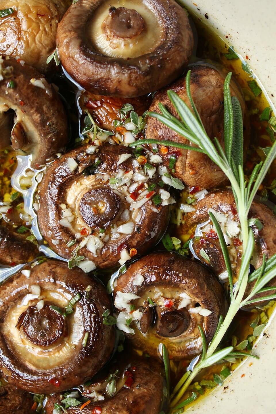 Close up of brown mushrooms and fresh rosemary sitting in a garlic and herb marinade.