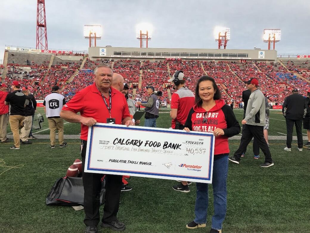 Two representatives hold a giant cheque showing food donation amount at Calgary Stampeders Game August 17, 2019