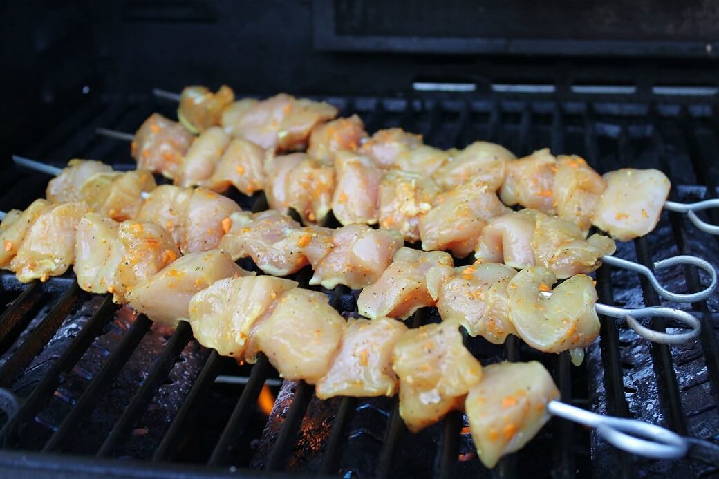 Raw marinated chicken kabobs on a grill.