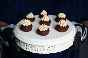 Seven bite sized black bean brownies topped with peanut butter frosting sit on a cream plate.