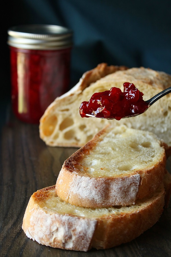 A spoon full of ruby red sour cherry jam poised above sourdough toast.