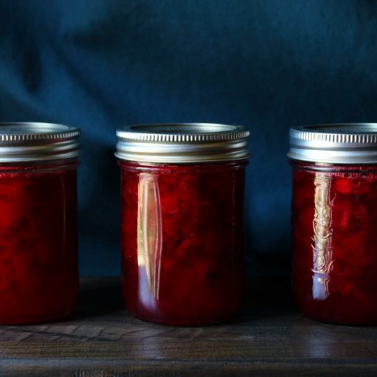 Three jars of ruby red sour cherry jam on a wooden board.