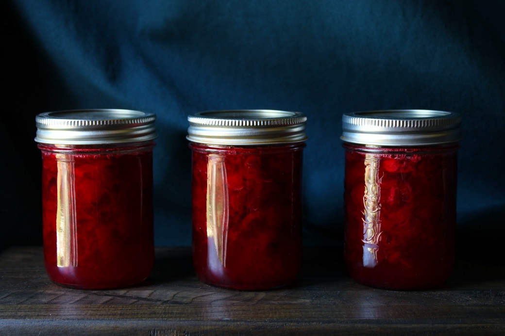Three jars of ruby red sour cherry jam on a wooden board.