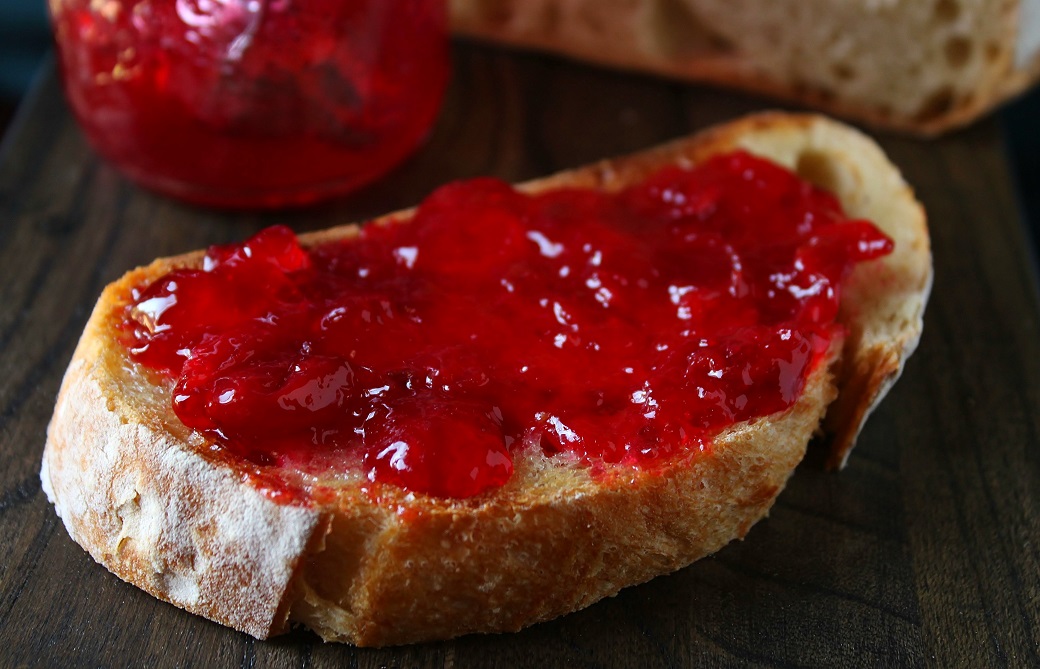 A slice of sourdough bread spread with ruby red sour cherry jam.