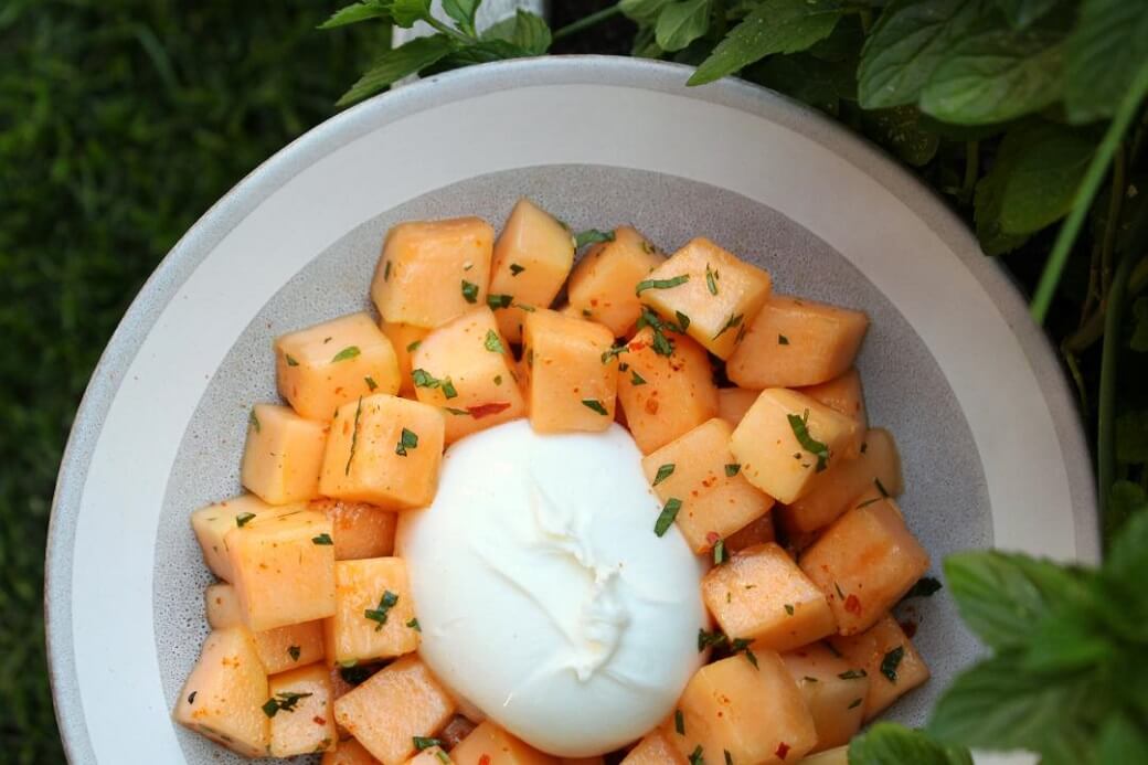 A white bowl containing Cantaloupe Salad with white burrata, mint, and chilies.