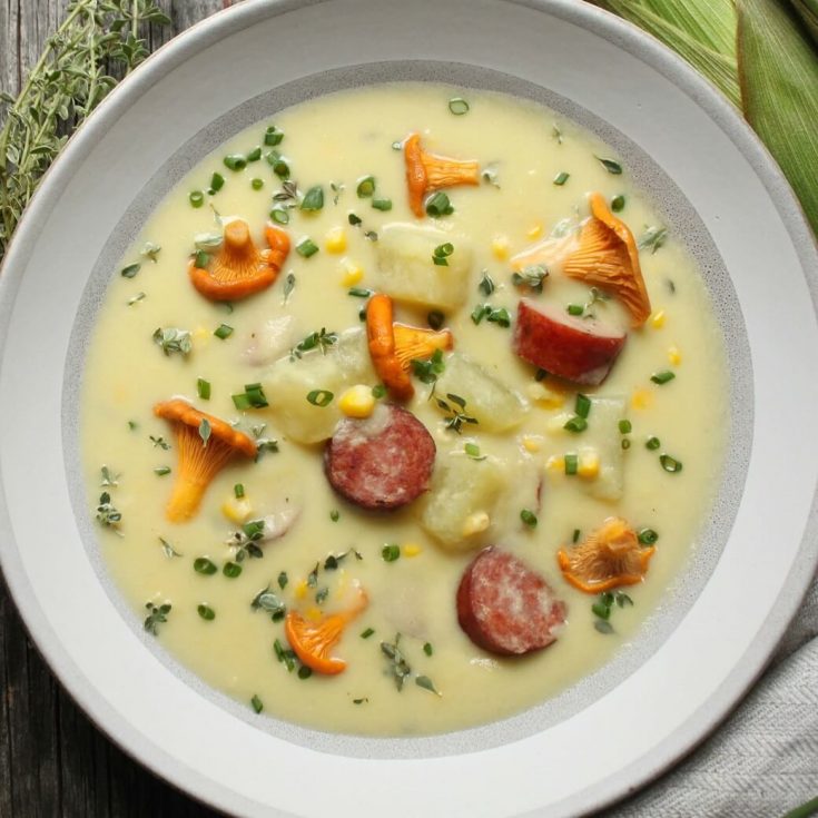 Hearty Farmer's Sausage Sweet Corn Chowder - Close up of a bowl of cream yellow soup with corn, sausage, potatoes and golden mushrooms garnished with fresh chives.