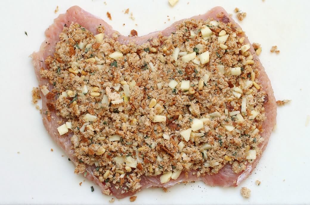 Apple Herb Stuffed Turkey Breast Recipe - A flat raw turkey cutlet topped with stuffing on a white cutting board.
