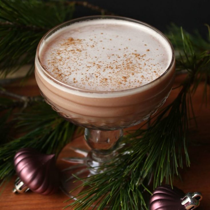 A mauve cocktail in a crystal coupe surrounded by fir branches and Christmas ornaments.