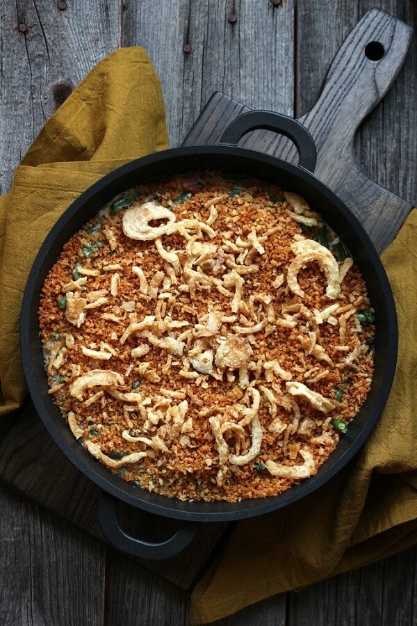 Overhead view of a golden topped Green Bean Casserole in a black dish on a wooden surface.