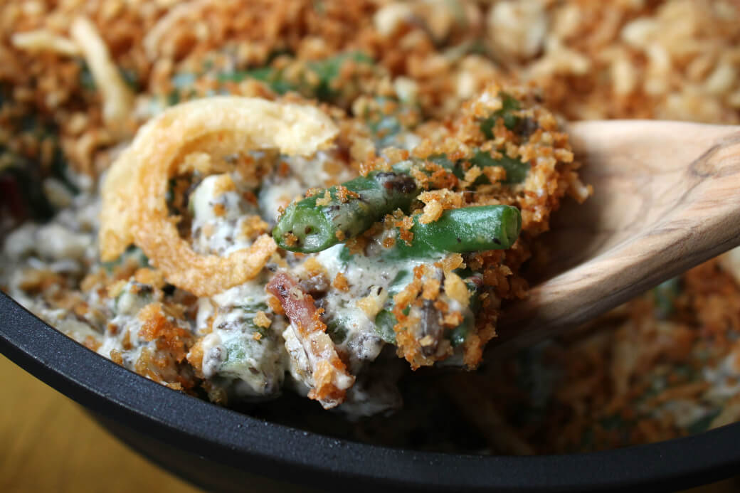 Close up of a spoonful of Green Bean Casserole showing green beans, bacon, mushrooms in a cream sauce. 