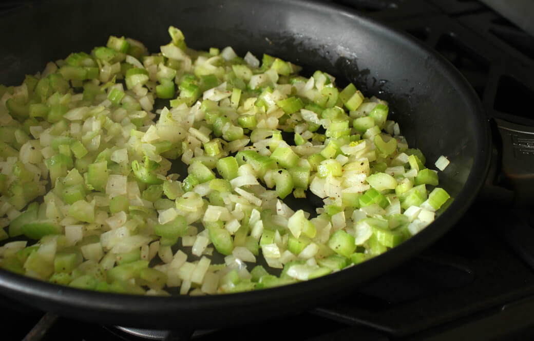 Celery and onions in a dark frying pan.