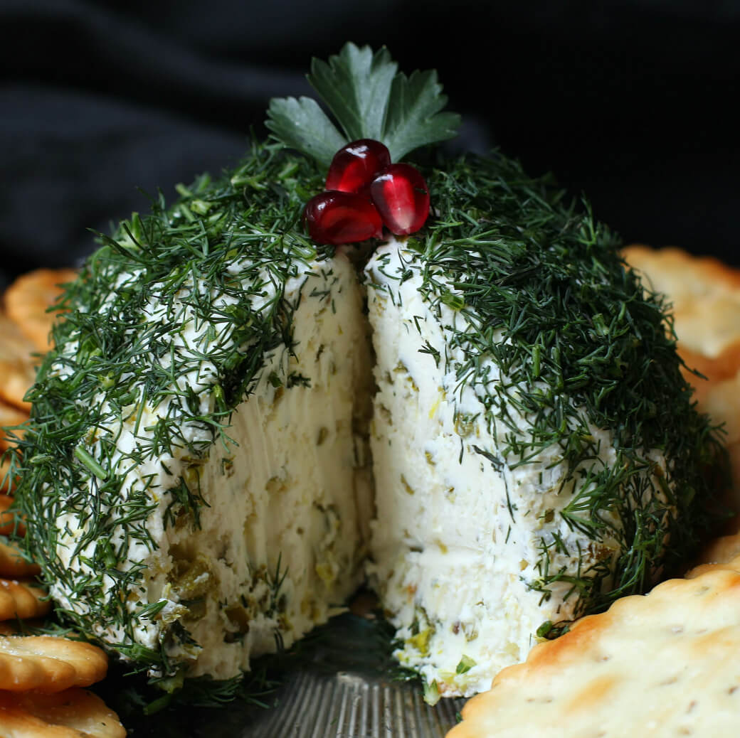 Dill Pickle Cheese ball - A cheese ball covered in fresh chopped dill with a slice missing sits in the middle of a circle of crackers.