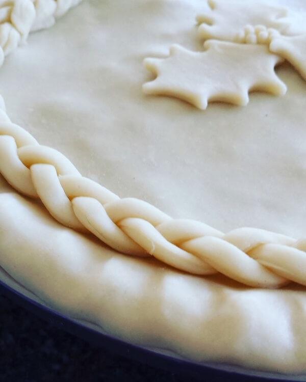 Christmas Eve Tourtière - Close up of unbaked pie with braided pastry and holly design.