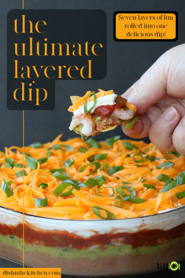 7 Layer Dip - Pinterest image of a hand holding a nacho chip topped with layered dip.