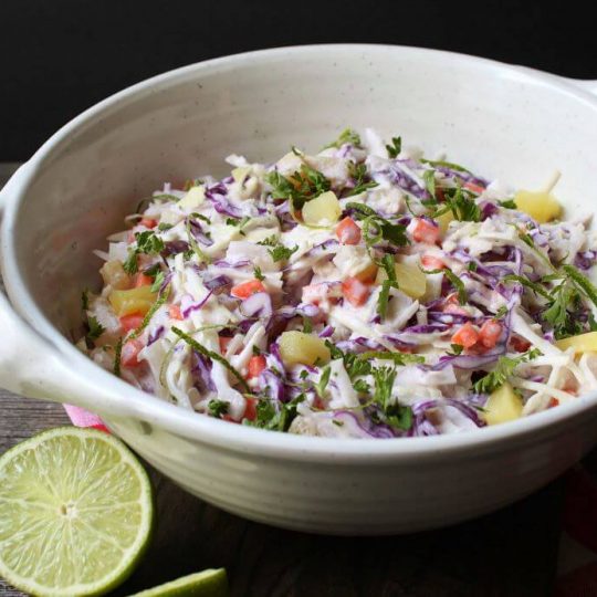 A multicoloured coleslaw with pineapple and lime in a white bowl.