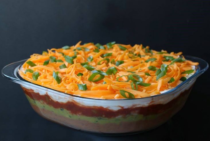 7 Layer Dip - A glass dish of layered dip topped with shredded cheese and sliced green onions.