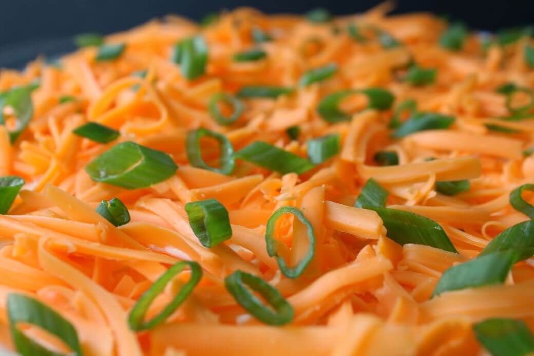7 Layer Dip - A close up shot of shredded cheese topped with sliced green onions.