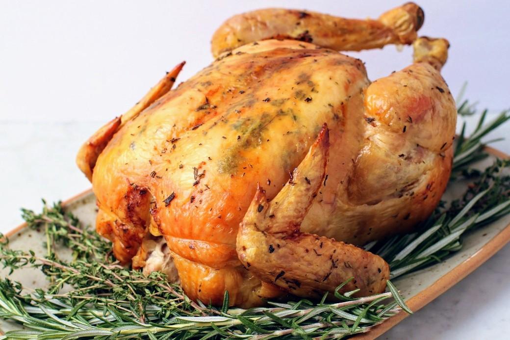 Dry Brine Chicken - A perfectly browned and roasted whole chicken sits on top of a bed of herbs.