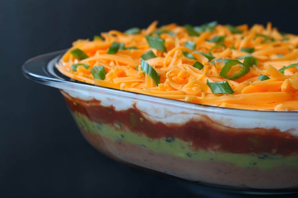 7 Layer Dip - A glass dish of layered dip topped with shredded cheese and sliced green onions. 