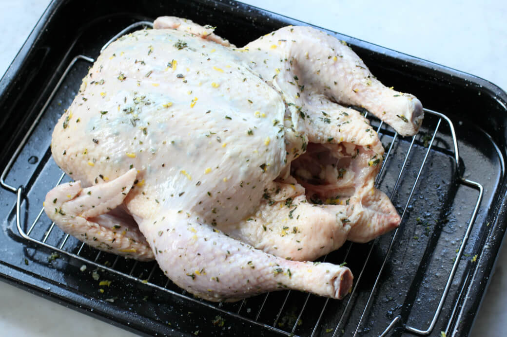 Dry Brine Chicken - A whole herb covered chicken sits inside a roasting pan.