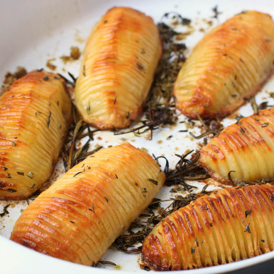 Crispy Herbed Hasselback Potatoes - Six crispy golden potatoes in a white baking dish.